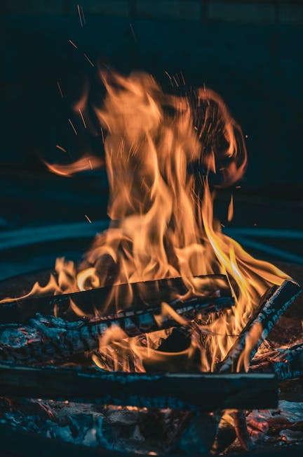 A glowing campfire with orange flames over charred wood logs